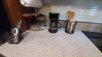 Una encimera de cocina con una cafetera, una cesta de utensilios y un control remoto.
