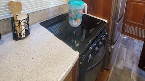 Una cocina con armarios de madera, microondas de acero inoxidable, estufa negra y refrigerador.