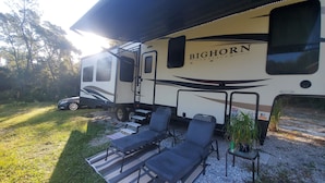 Una caravana Bighorn Traveler con un porche cubierto que incluye mobiliario de exterior y una pequeña mesa.