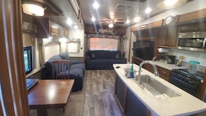Interior compacto de una caravana, con kitchenette, zona de estar y televisión.