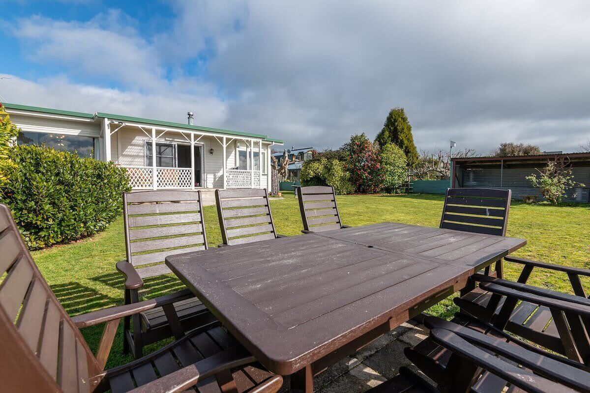 A picnic table with benches in a grassy area with a house in the background.