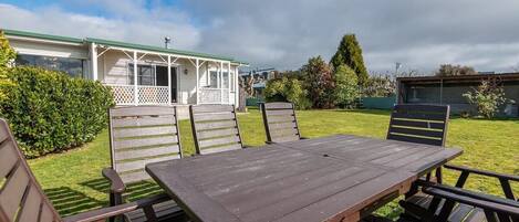 A picnic table with benches in a grassy area with a house in the background.