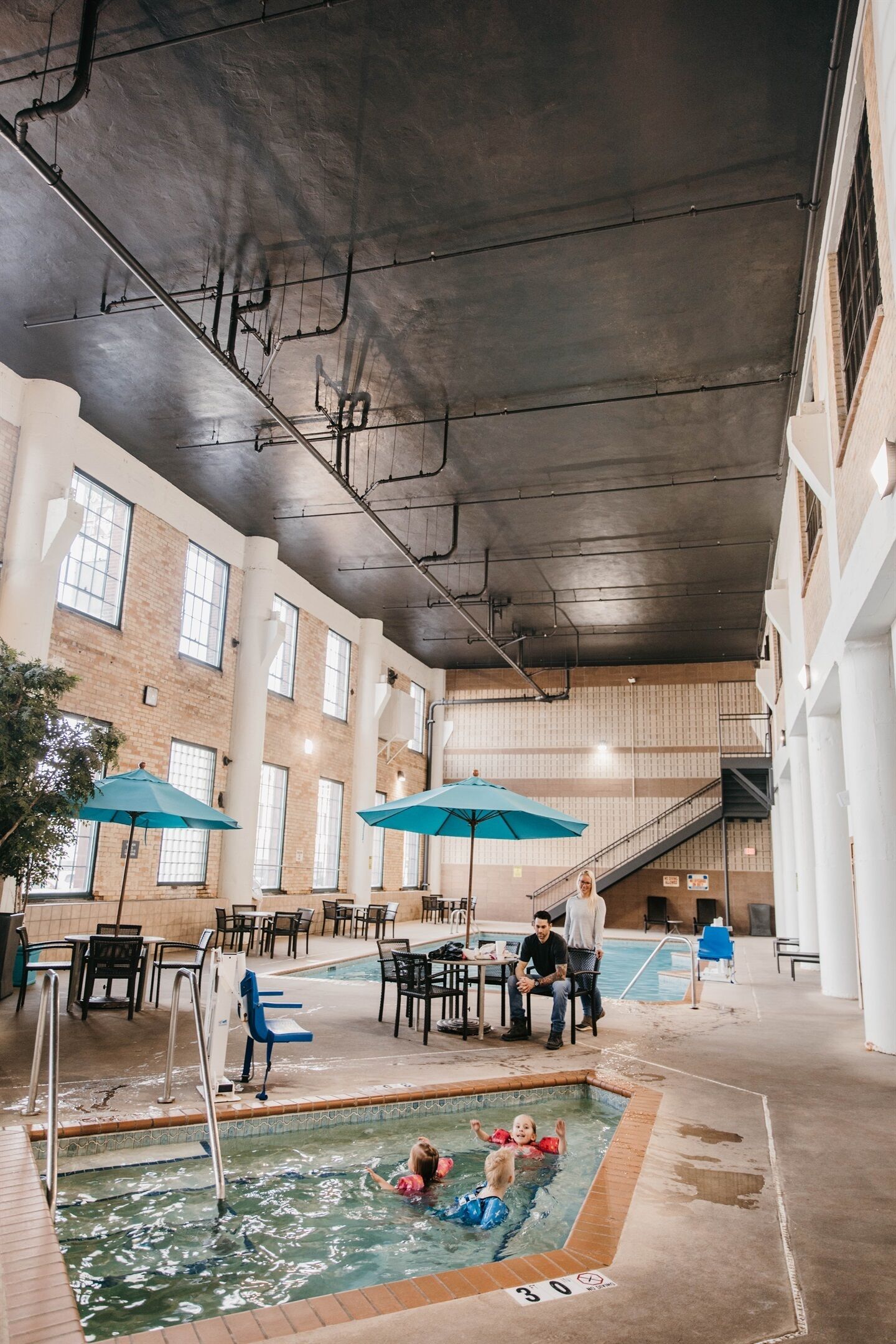 An indoor swimming pool area with a pool, lounge chairs, and umbrellas.