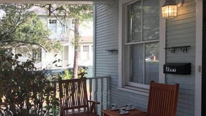 A porch with two wooden chairs and a table, a potted plant, and a mailbox.