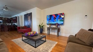 A living room with a TV, a red sofa, a coffee table, and a kitchen in the background.