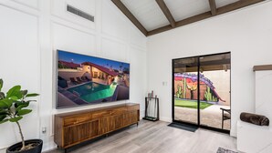 A spacious living room with a large TV, wooden entertainment unit, and a sliding glass door leading to an outdoor area.