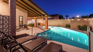 A swimming pool with lounge chairs and a covered seating area.