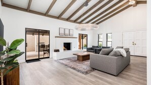 A spacious living room with a fireplace, a grey sofa, and a large window.