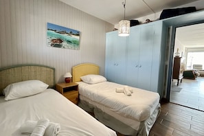 A hotel room with two beds, a wardrobe, a painting of a beach scene, and a hanging light fixture. - Appt Avec vue Exceptionnelle sur la Baie + Garage (Le Crotoy)