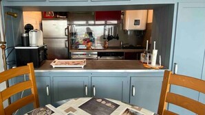 A compact kitchen with light blue cabinets, a stainless steel refrigerator, and a wooden dining table with chairs.
