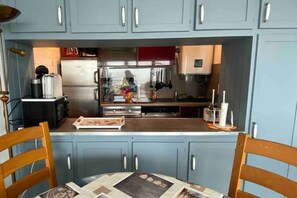 A compact kitchen with light blue cabinets, a stainless steel refrigerator, and a wooden dining table with chairs. - Appt Avec vue Exceptionnelle sur la Baie + Garage (Le Crotoy)