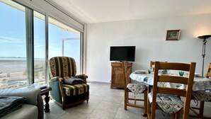 A spacious room with a large window, a television, a dining table, and a sofa.