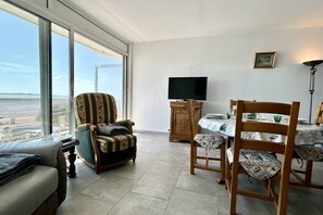 A spacious room with a large window, a television, a dining table, and a sofa. - Appt Avec vue Exceptionnelle sur la Baie + Garage (Le Crotoy)