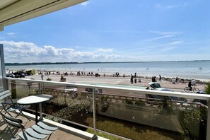 En balkong med utsikt över en strand, utomhusmöbler och en klar himmel.