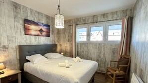 A bedroom with a bed, bedside table, chair, window, and a painting on the wall.