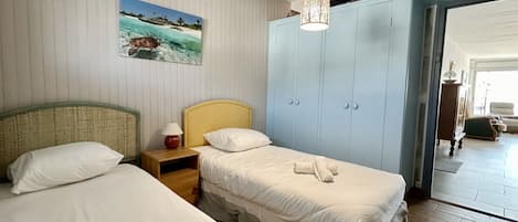Habitación de hotel con dos camas, un armario, un cuadro de una playa y una lámpara colgante.