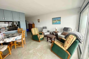 A living room with a dining table, chairs, a sofa, a small table, and a window. - Appt Avec vue Exceptionnelle sur la Baie + Garage (Le Crotoy)