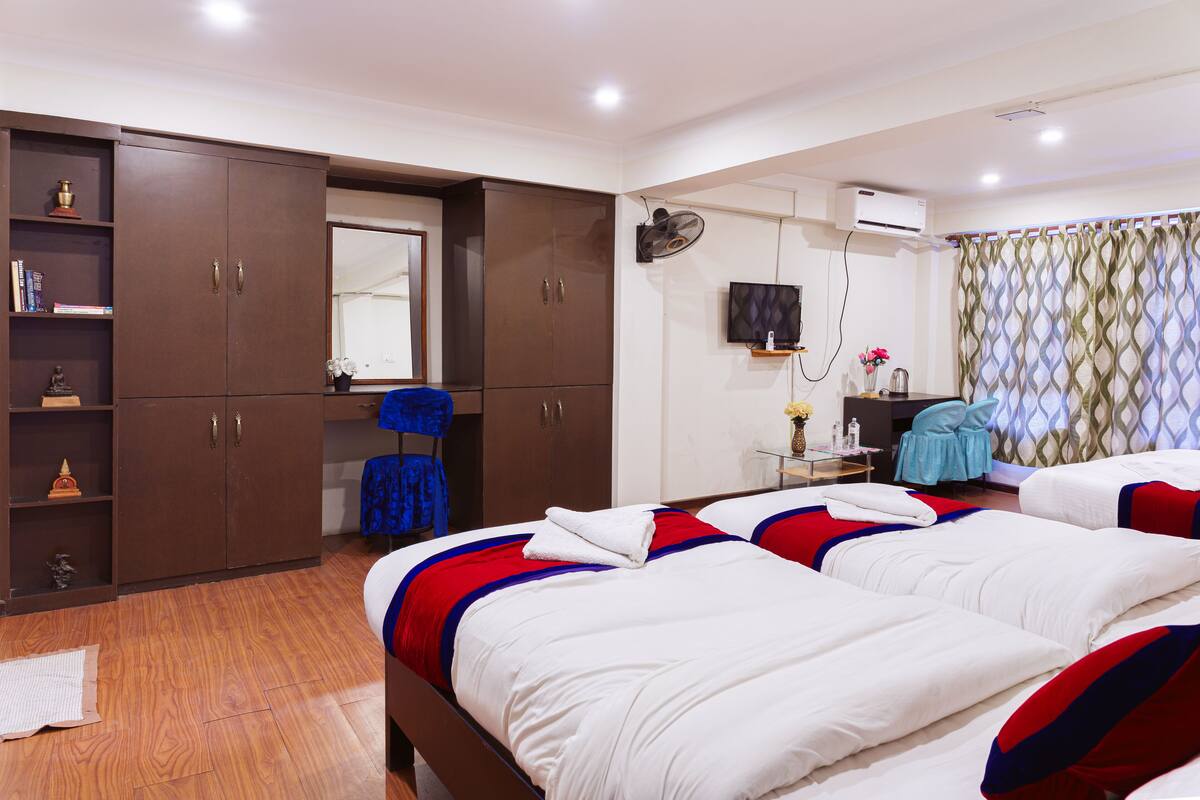 A hotel room with two beds, a wardrobe, a mirror, a desk with a chair, and a window with curtains.