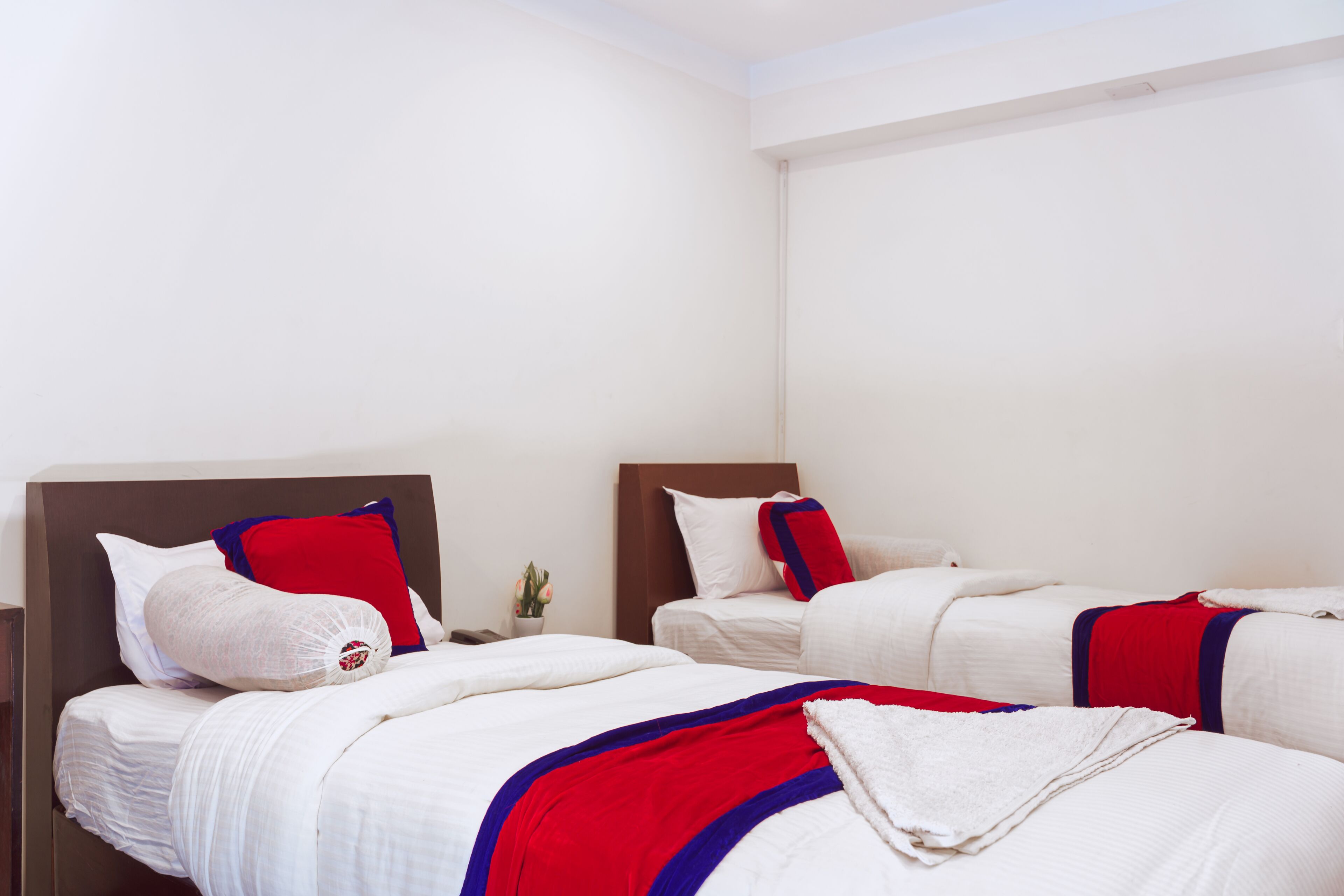 Hotellihuone, jossa on kaksi sänkyä. Jokaisessa sängyssä on valkoiset vuodevaatteet, ja niissä on punaisia ja sinisiä yksityiskohtia sekä puinen pääty.
