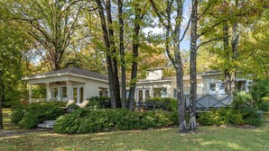 A two-story house with a covered porch and a deck, surrounded by mature trees and well-maintained lawns. - Moonlight Baydream: Lakefront Home w/ Private Dock, Large Patio, Fast WiFi & Near Oaklawn & Downtown (Hot Springs)