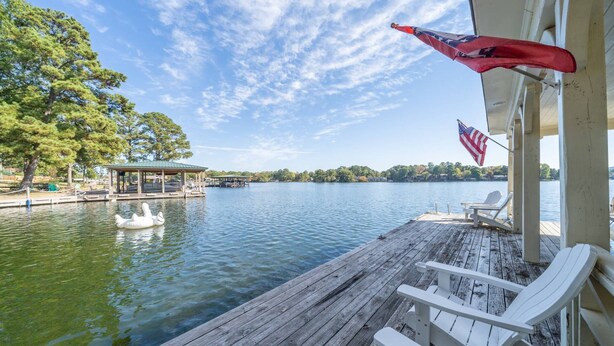 A wooden dock with white chairs, a swan float, and an American flag. - Moonlight Baydream: Lakefront Home w/ Private Dock, Large Patio, Fast WiFi & Near Oaklawn & Downtown (Hot Springs)