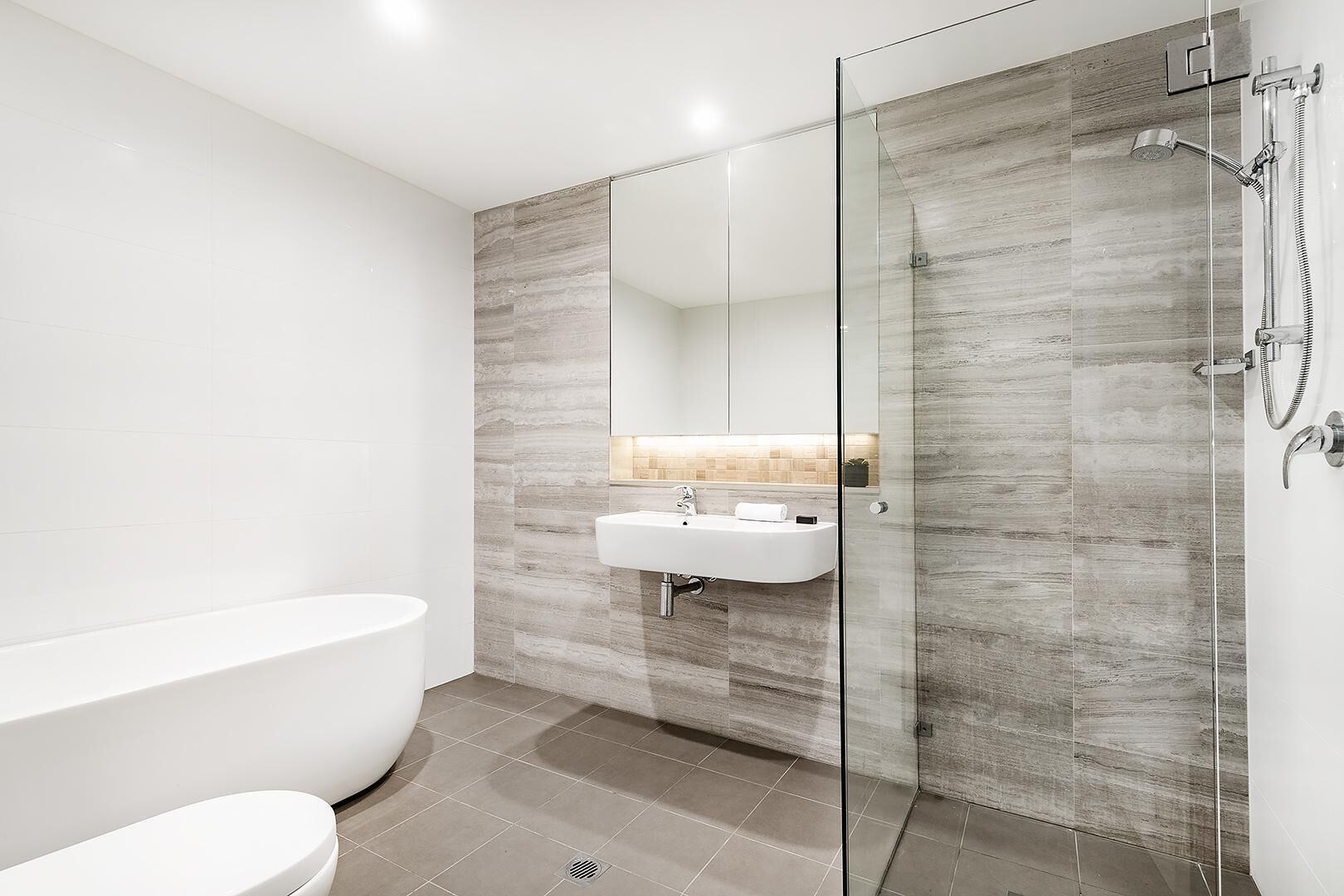 Een moderne badkamer met een vrijstaand bad, een douche met glazen wanden en een wit wastafelmeubel met spiegel.