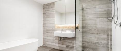 Een moderne badkamer met een vrijstaand bad, een douche met glazen wanden en een wit wastafelmeubel met spiegel.