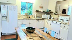 Een keuken met witte kastjes, een houten eettafel met stoelen, een magnetron en een fornuis.