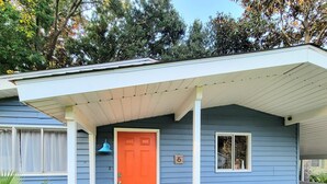 Een huis met een blauwe gevel, een rode deur en een veranda met een bankje en een tafeltje.