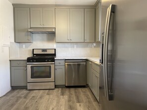 A kitchen with grey cabinets, a stainless steel refrigerator, a dishwasher, and a stove.