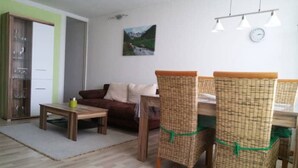 Un coin repas avec des chaises en osier, une table en bois et un canapé. Un tableau est accroché au mur et une horloge se trouve au-dessus de la table.