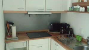Une cuisine de taille réduite avec des meubles blancs, un plan de travail en bois, une machine à café et un égouttoir à vaisselle.