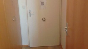 Un couloir étroit, avec une porte en bois au fond, une petite marche et un paillasson.
