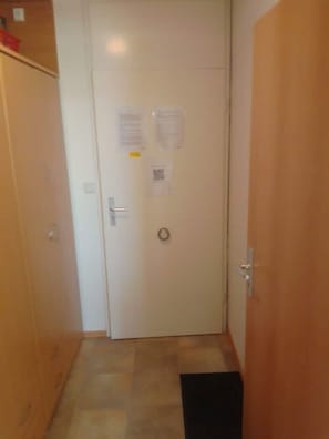 A narrow hallway with a wooden door at the end, a small step, and a doormat.