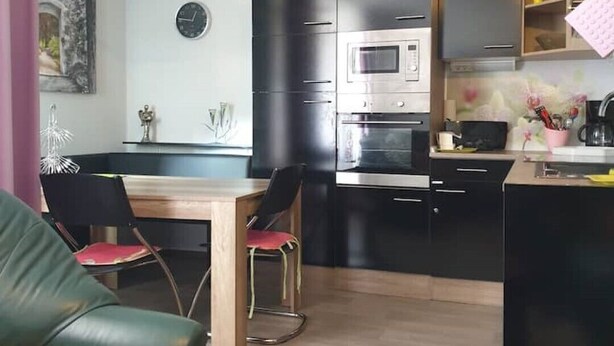 A modern kitchen with black cabinets, a microwave, and a stove. There is a dining area with a table and chairs. - FeWo Regenbogen. a colorful start to every day! (Altenau)