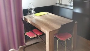 A modern kitchen with a wooden table, red chairs, a black refrigerator, and a wall-mounted clock. - FeWo Regenbogen. a colorful start to every day! (Altenau)