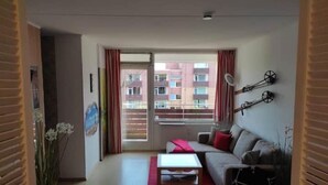 A modern living room with a sofa, a coffee table, and a view of a building through a large window. - FeWo Schneeglocke The cozy little room! (Altenau)