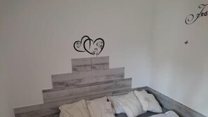 A bedroom with a bed, a small stool, and a wall with a heart design. - FeWo Schneeglocke The cozy little room! (Altenau)