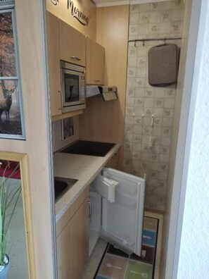A compact kitchen with wooden cabinets, a microwave, a small refrigerator, and a tiled backsplash.