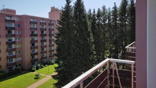 A residential building with multiple balconies, surrounded by tall evergreen trees and a well-maintained lawn. - FeWo Schneeglocke The cozy little room! (Altenau)
