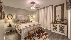 Ein Schlafzimmer mit einem hölzernen Bett, einer Bank, einem Kuhfellteppich, einem Deckenventilator, einem Spiegel und einem Schrank.