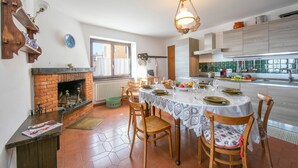 Un coin repas agrémenté d’une cheminée en briques, de chaises en bois, d’une table dressée pour quatre personnes et d’une vue sur la cuisine.