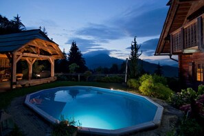 A swimming pool with a wooden deck, surrounded by a garden and a mountain view. - Chalet Podgorje With Pool (Slovenj Gradec)