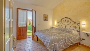 Un dormitorio con cama, una puerta que da a un balcón, una lámpara de pared y un estante pequeño.