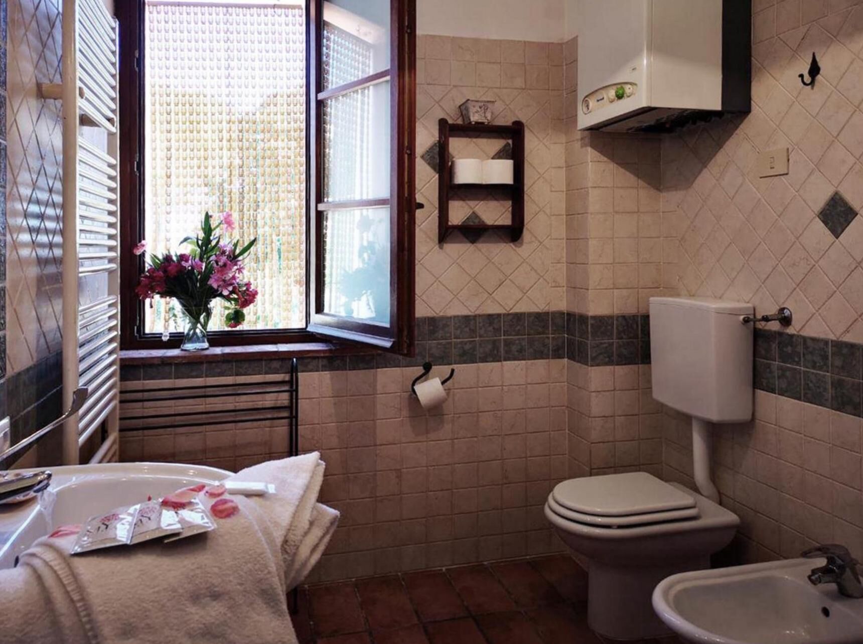 A bathroom with a toilet, bidet, and a window with flowers.