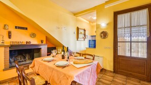 A dining area with a table set for four, a fireplace, and a door with patterned curtains. - Olive apt With Shared Pool (Castiglione del Lago)