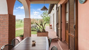 A patio with a table and chairs, a hanging light fixture, and a view of the garden. - Olive apt With Shared Pool (Castiglione del Lago)