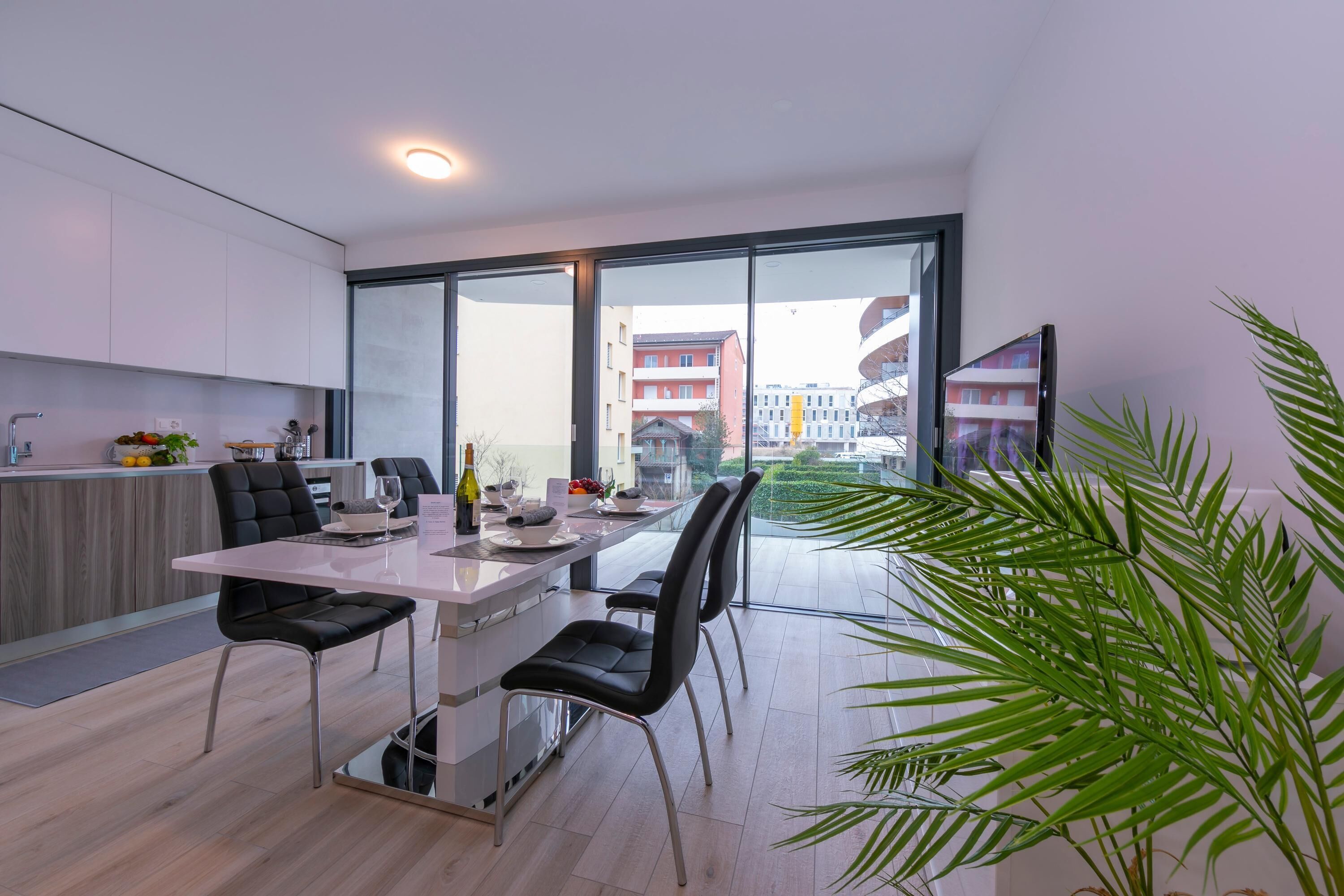 A modern kitchen with a dining area, large windows, and a view of buildings.