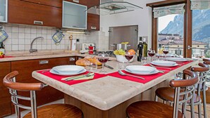 A kitchen with a central island, bar stools, and a view of a mountain. - Paulie Apartment in Riva del Garda (Riva del Garda)