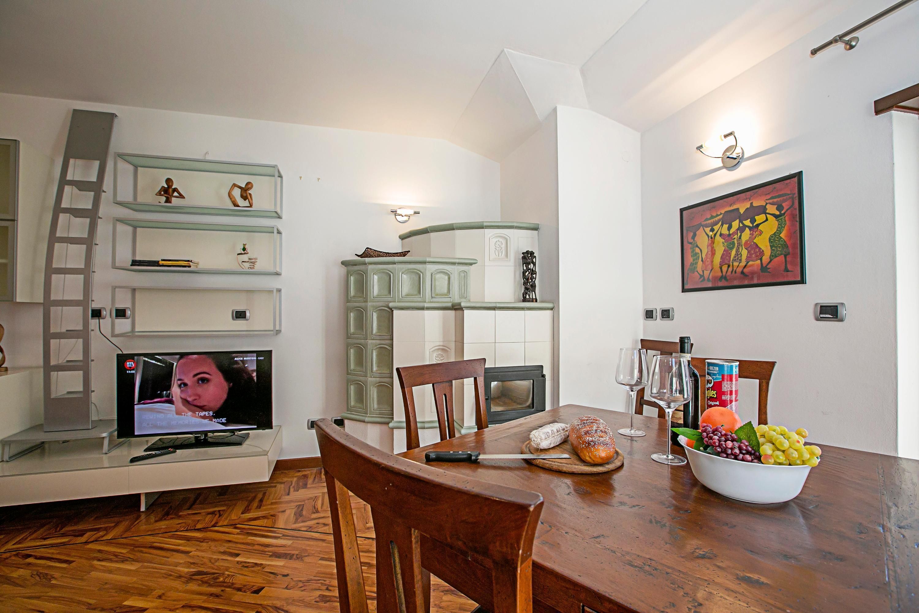 A modern kitchen with a dining table set for two, a TV, and a fruit bowl.